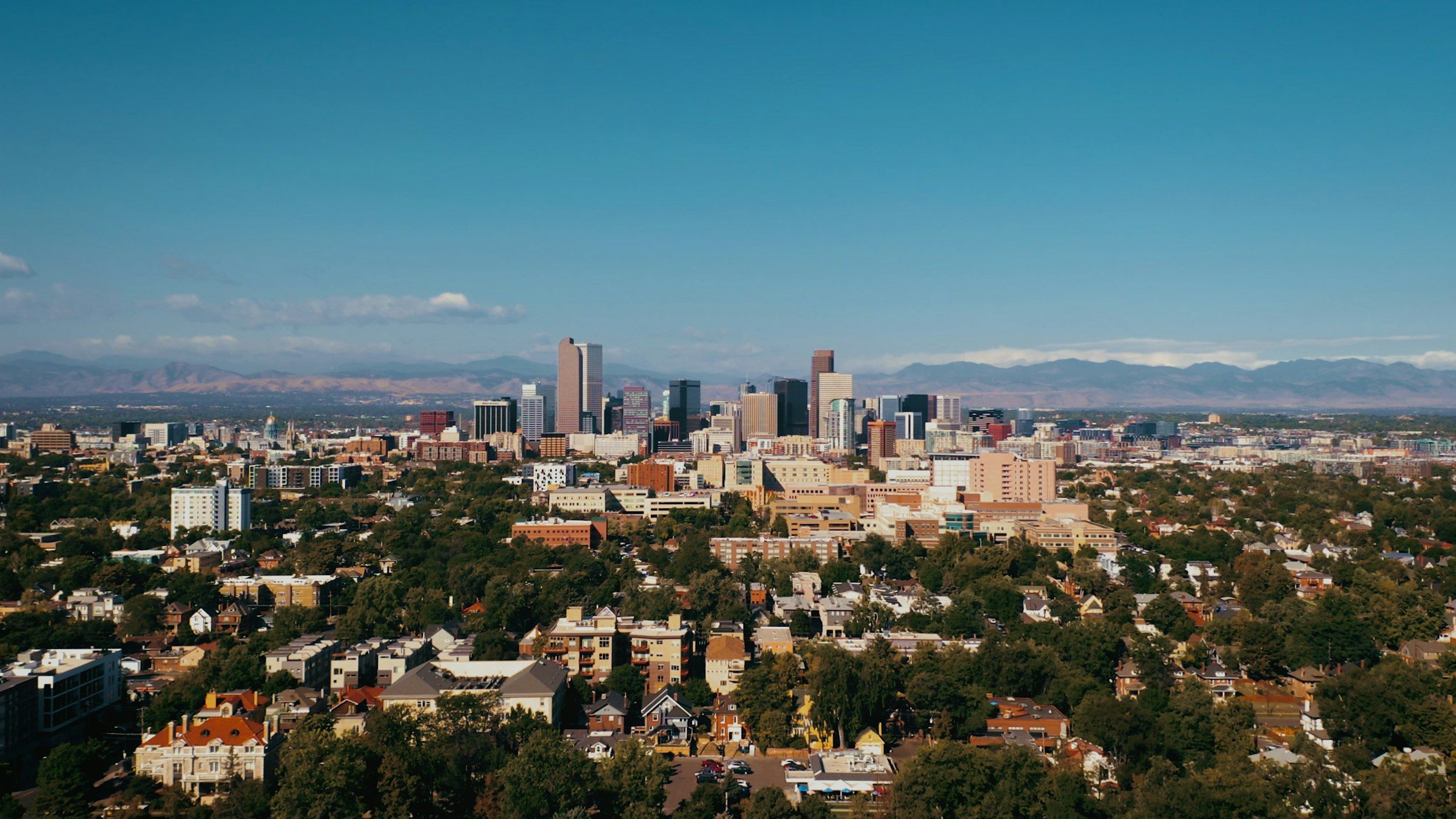 Downtown Denver rising above tree-lined neighborhoods, with the Front Range on the horizon