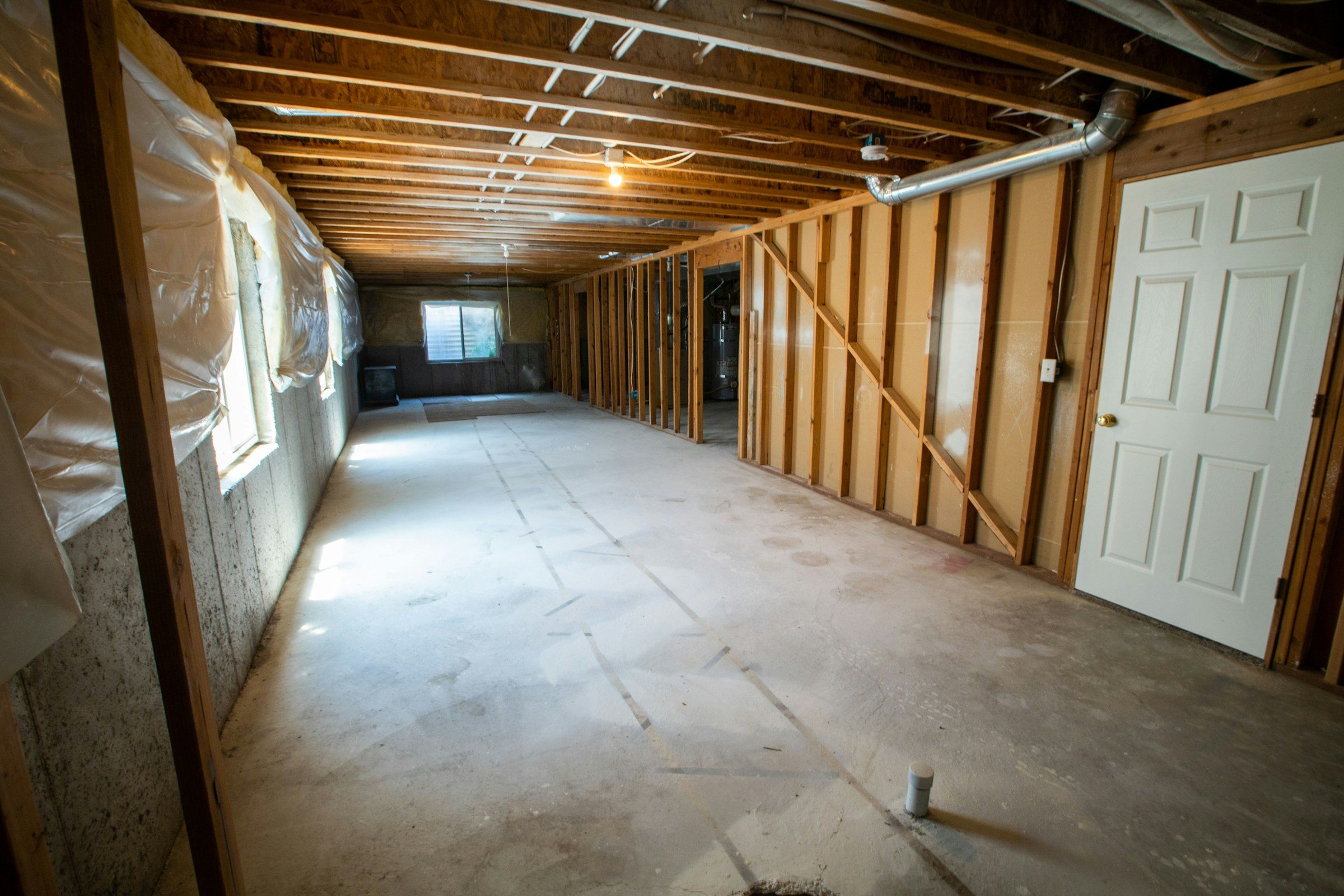 An unfinished basement with exposed floor joists, new stud walls and a bare concrete slab