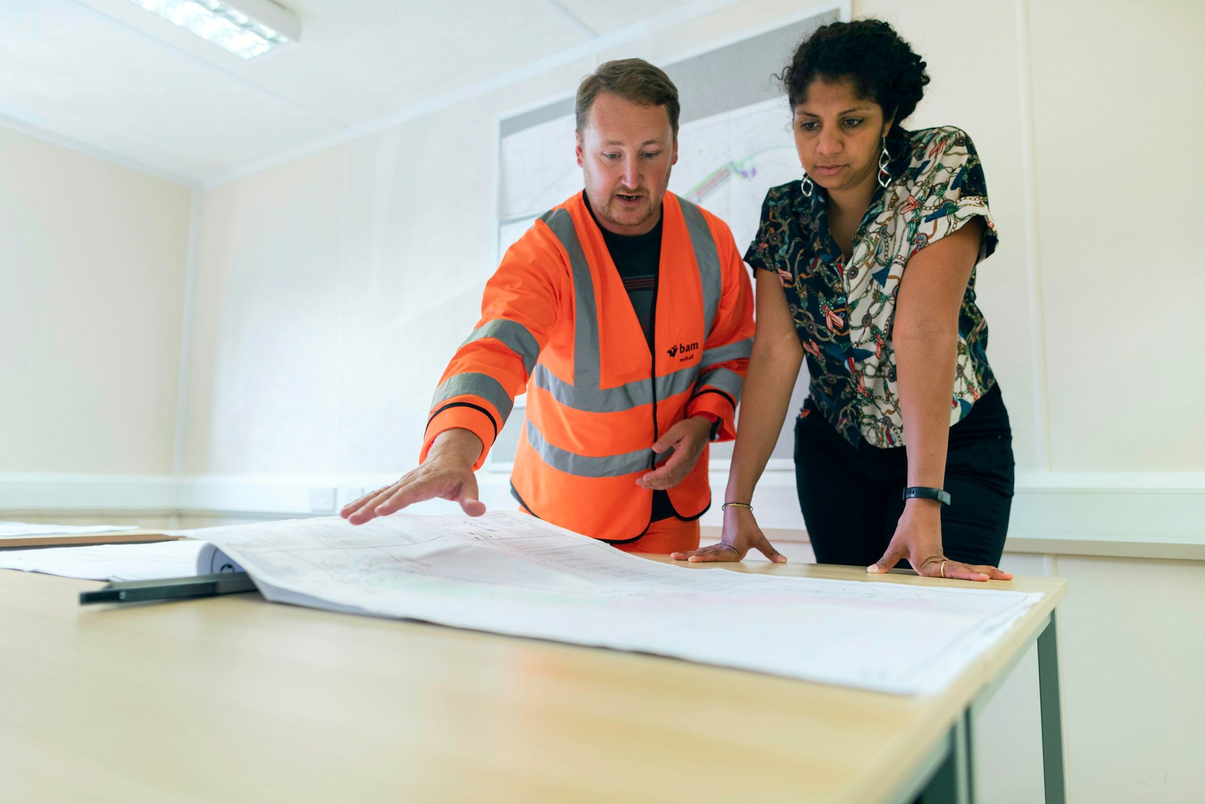 Two people leaning over a set of drawings spread across a table