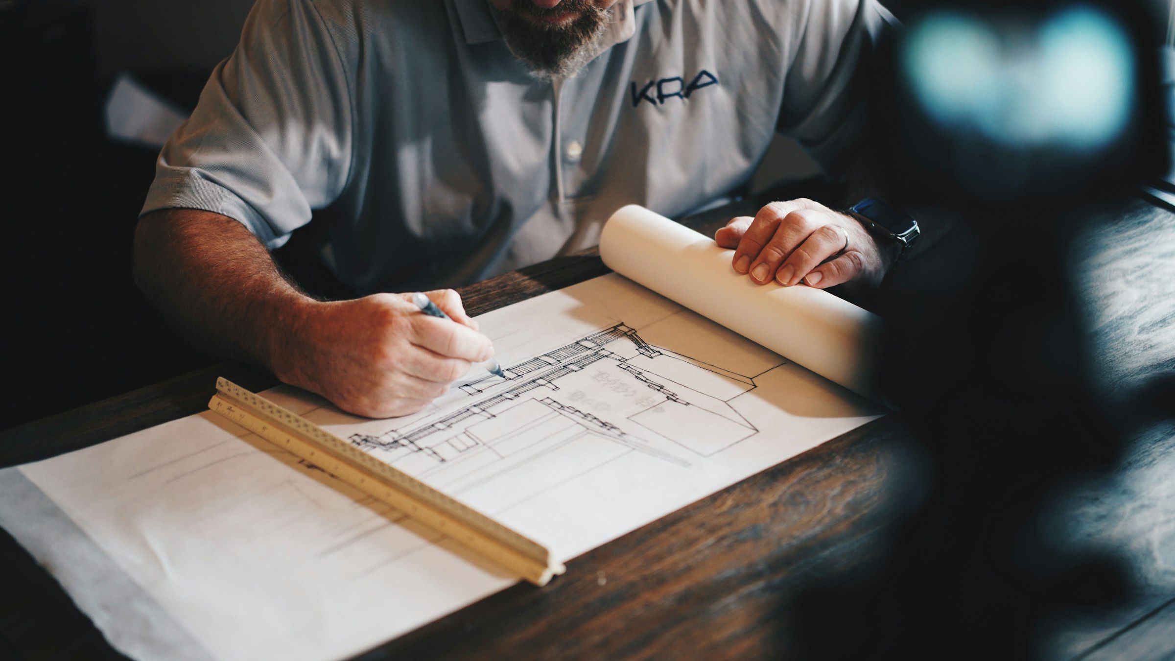 An engineer drafting a detail by hand with a pencil and a wooden rule