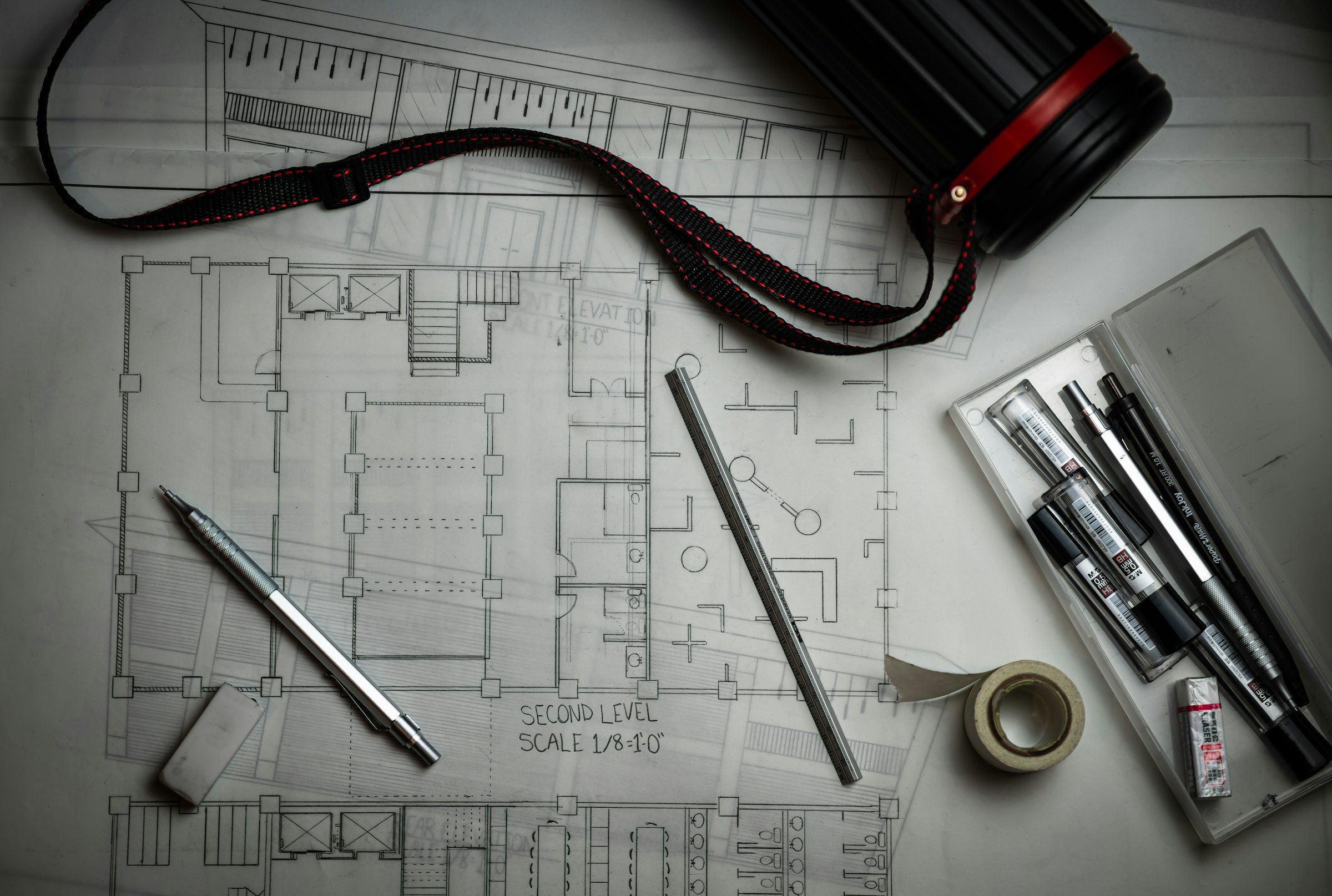 Architectural floor plans with drafting pencils, a steel rule and a drawing tube