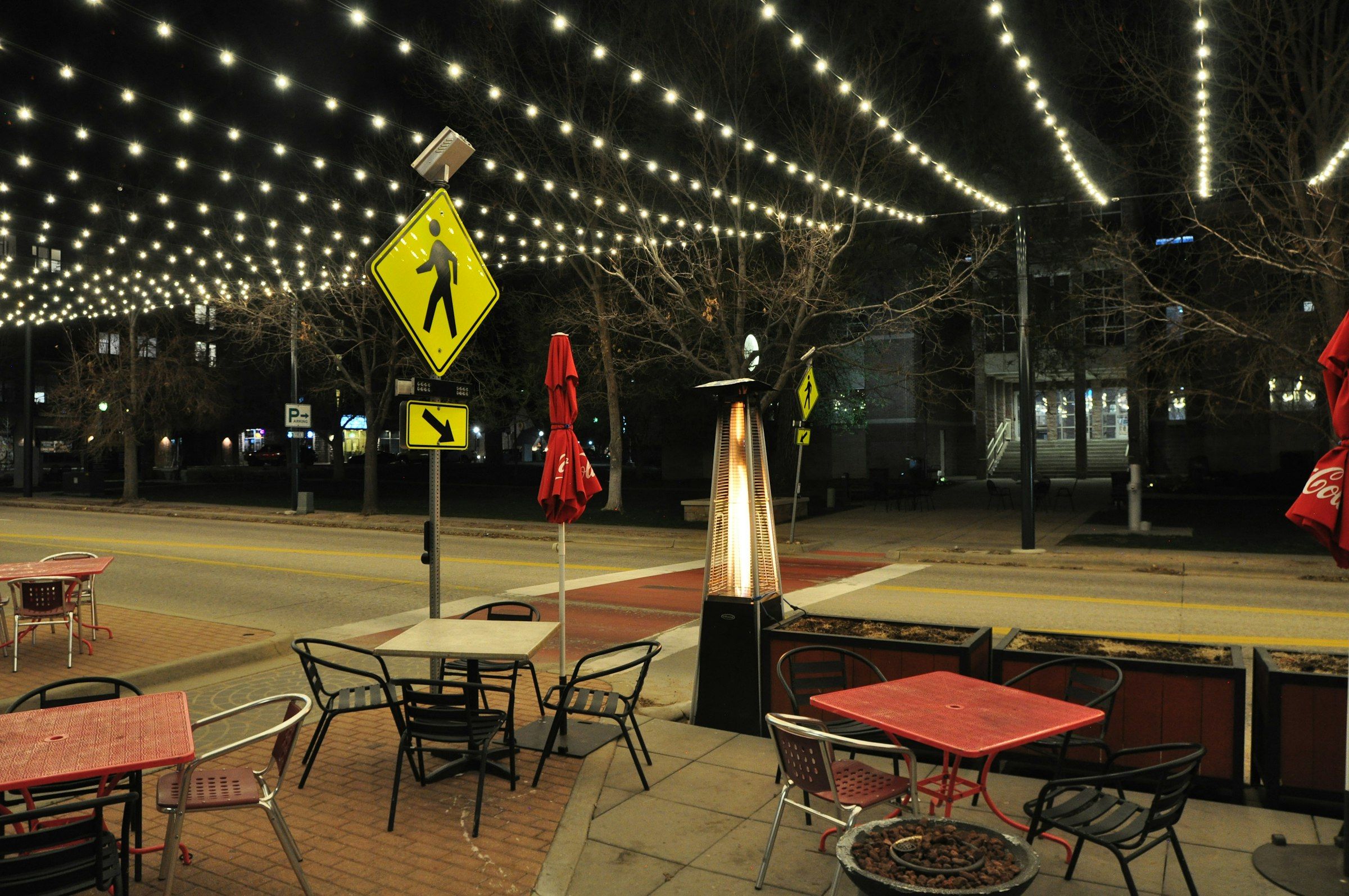 Patio tables under strings of lights on a plaza in Castle Rock at night
