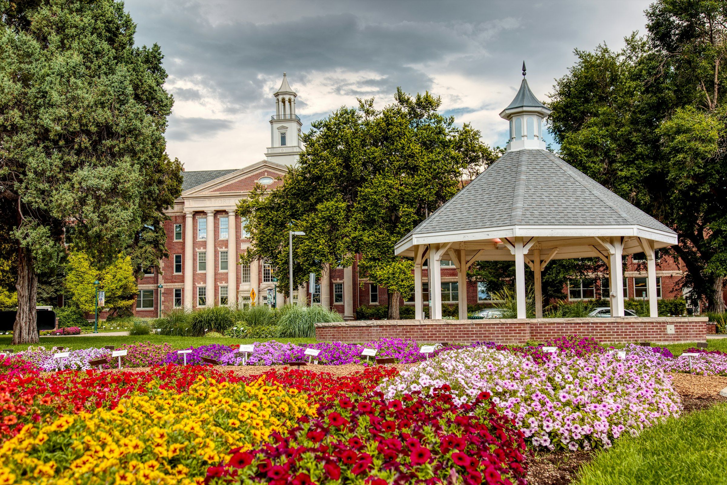 Flower beds and a white gazebo in front of a brick building in Fort Collins