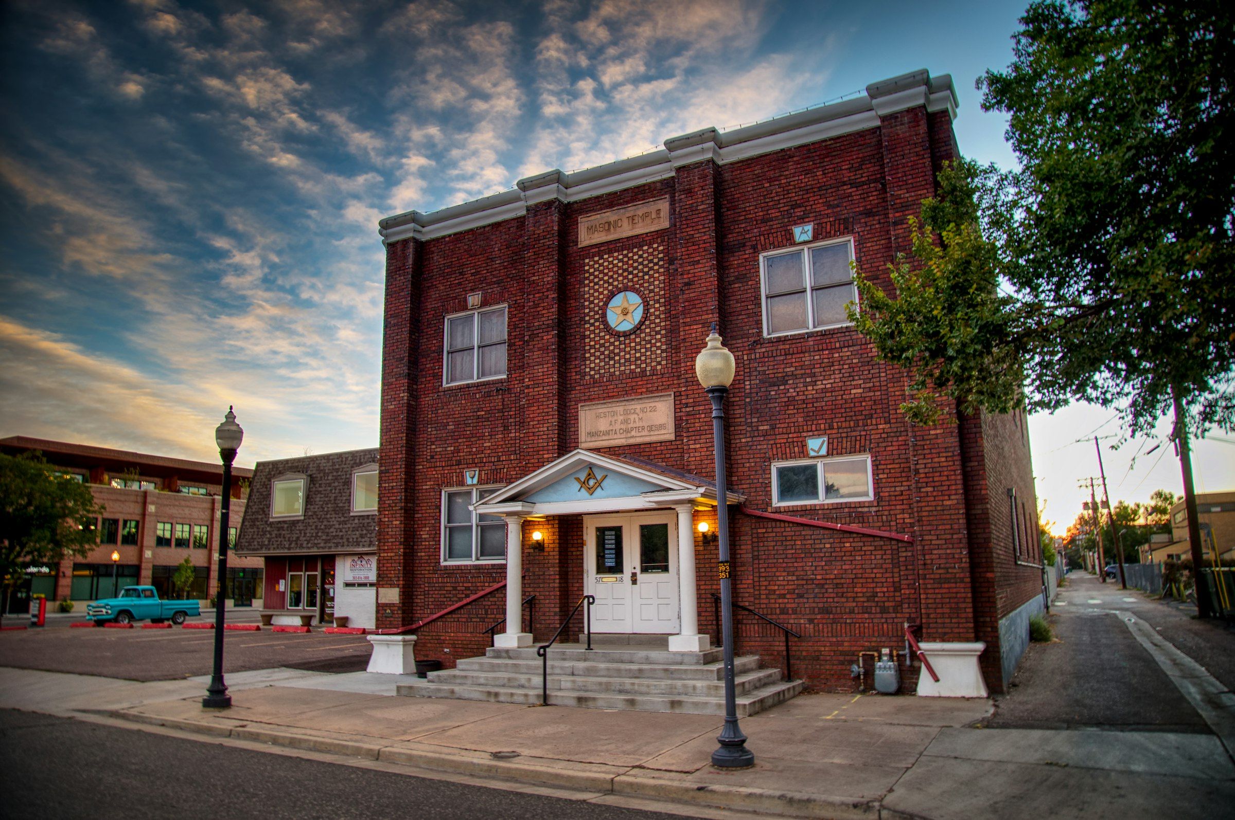 A red brick building with a clock and a columned entry on a Littleton street at dusk