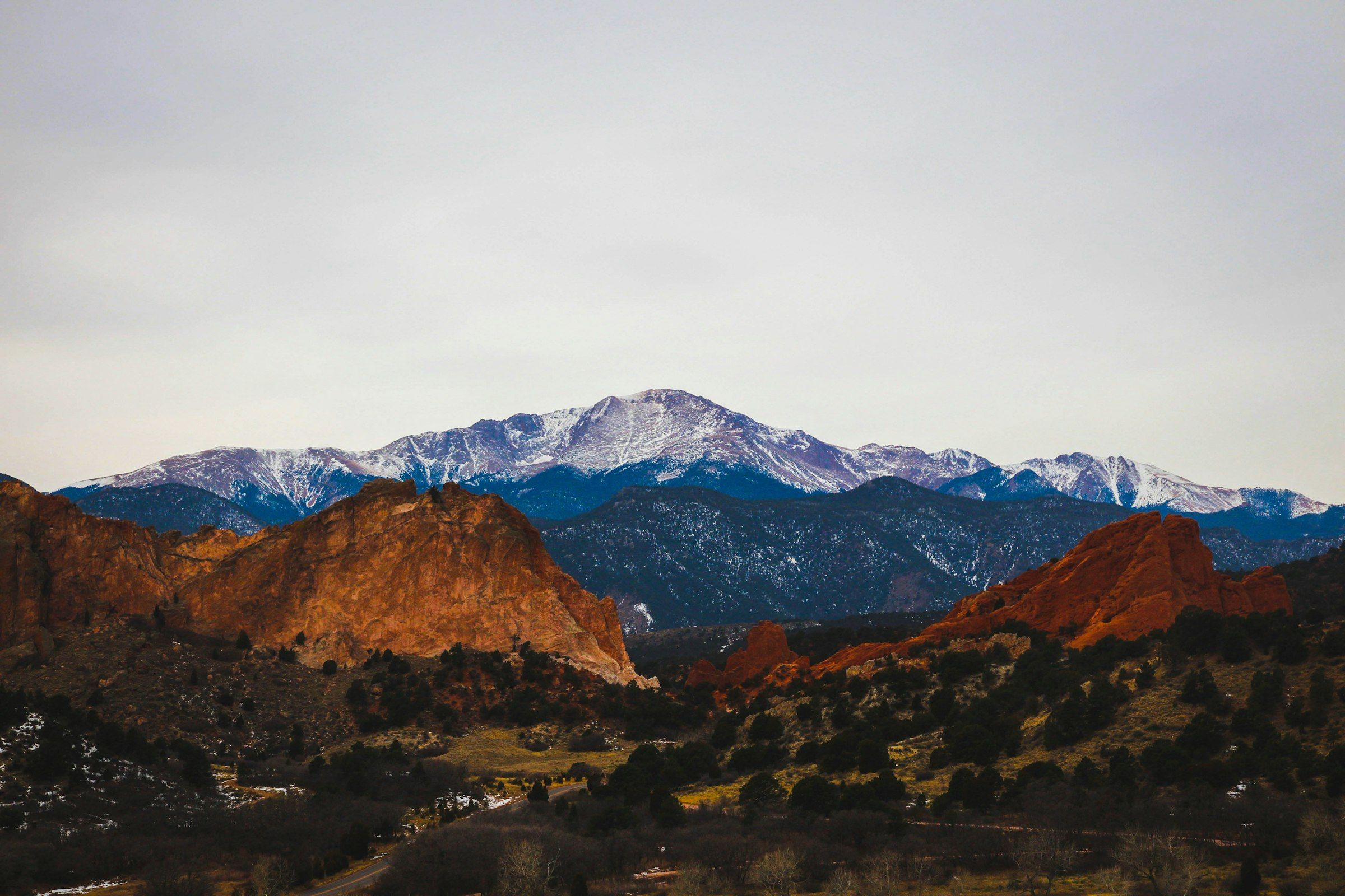 Pikes Peak with snow on its summit, rising above red rock ridges near Colorado Springs