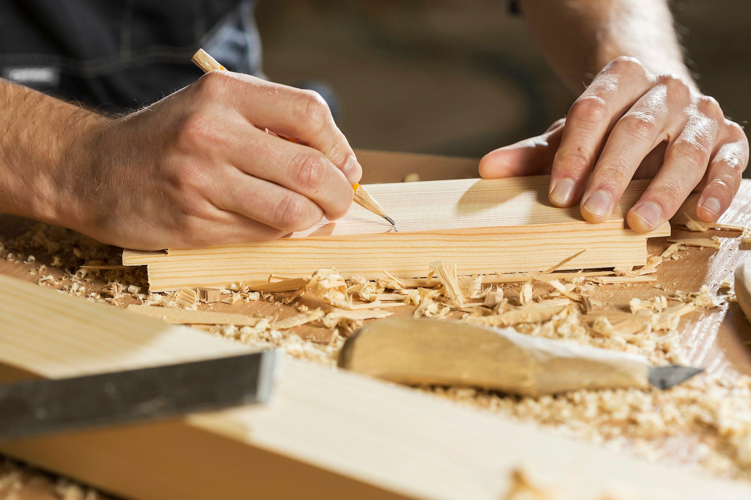 Hands marking a line on a board with a pencil, wood shavings on the bench