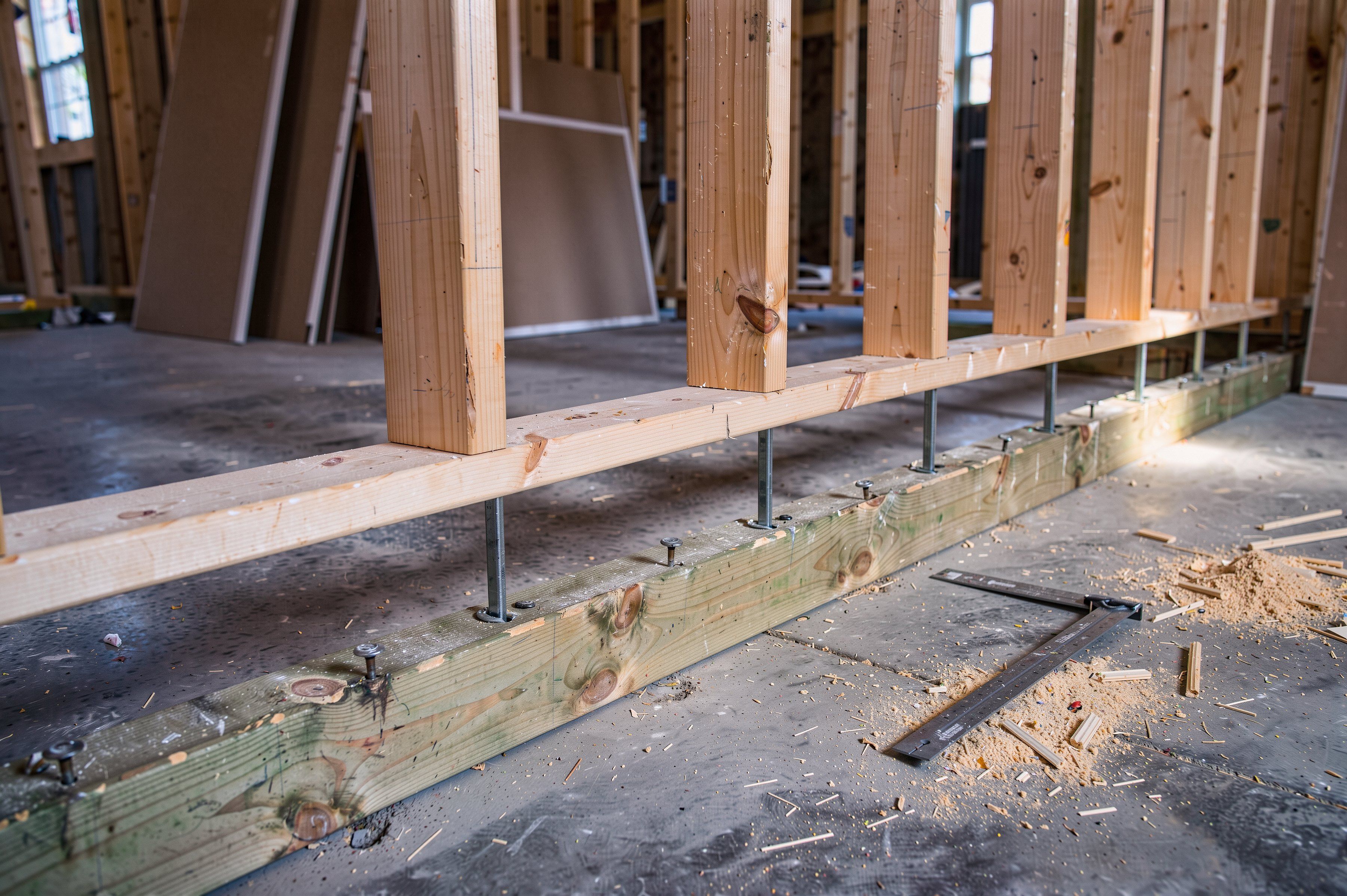 A floating wall under construction: a treated plate fastened to the concrete slab, a gap, and steel spikes guiding the hanging wall plate above