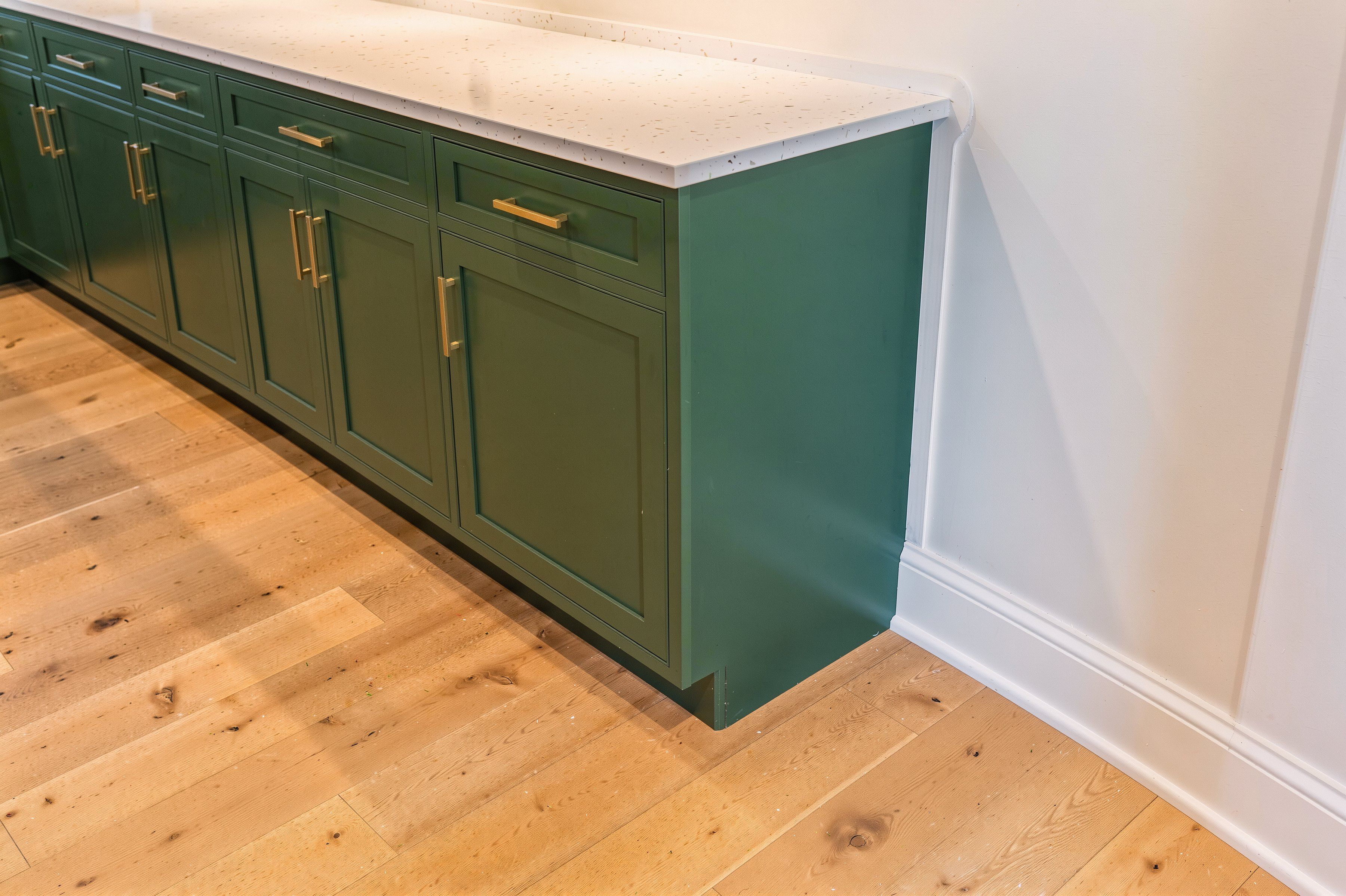 Evergreen shaker base cabinets with brass pulls and a white quartz top, the end panel scribed tight to the side wall