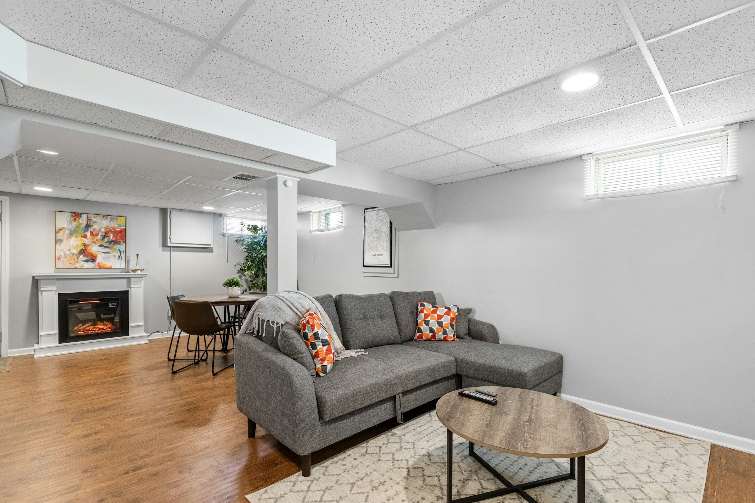 A finished basement family room with a sectional, a fireplace wall and small windows high on the wall