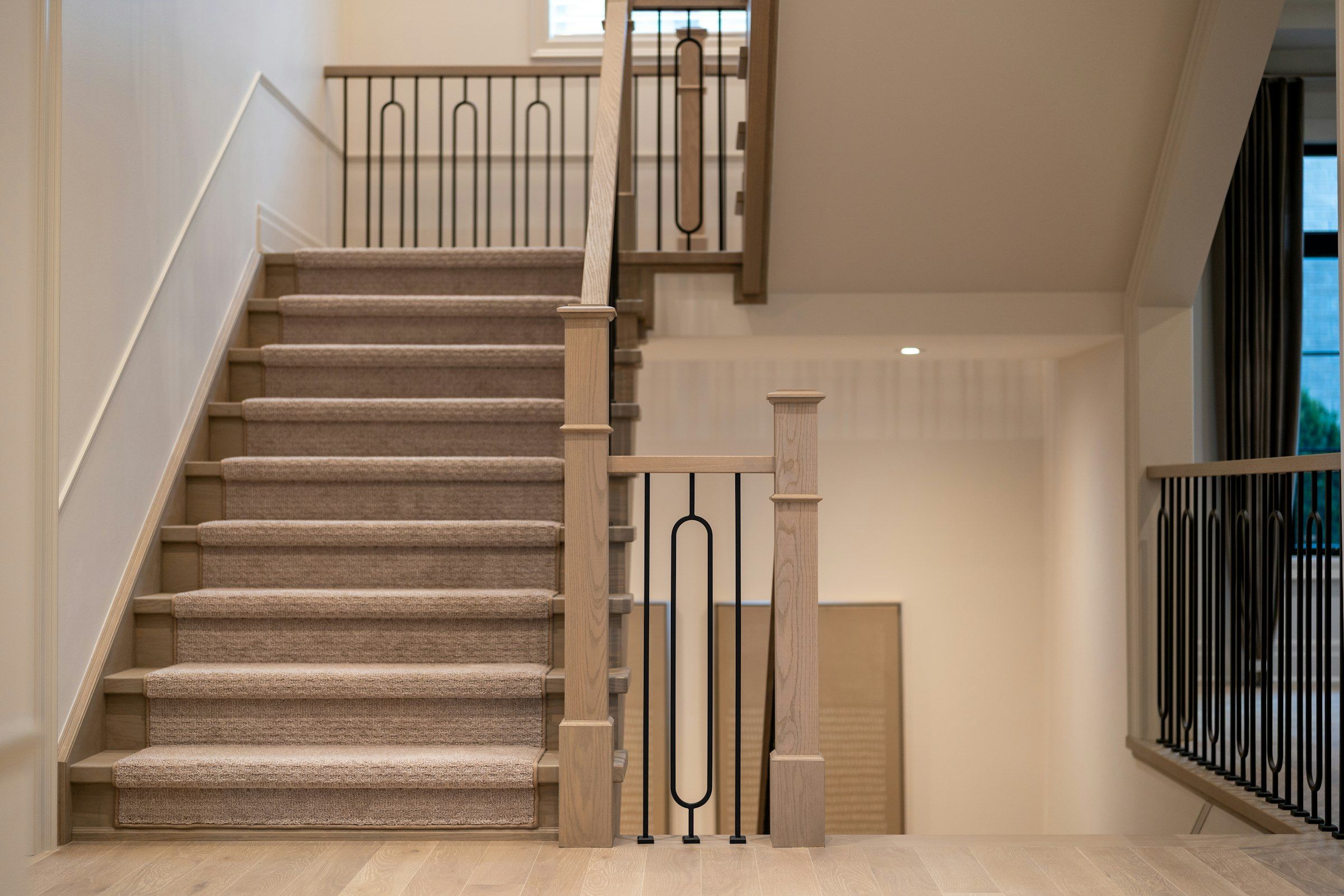 A carpeted staircase with a black steel rail leading down to a finished lower level