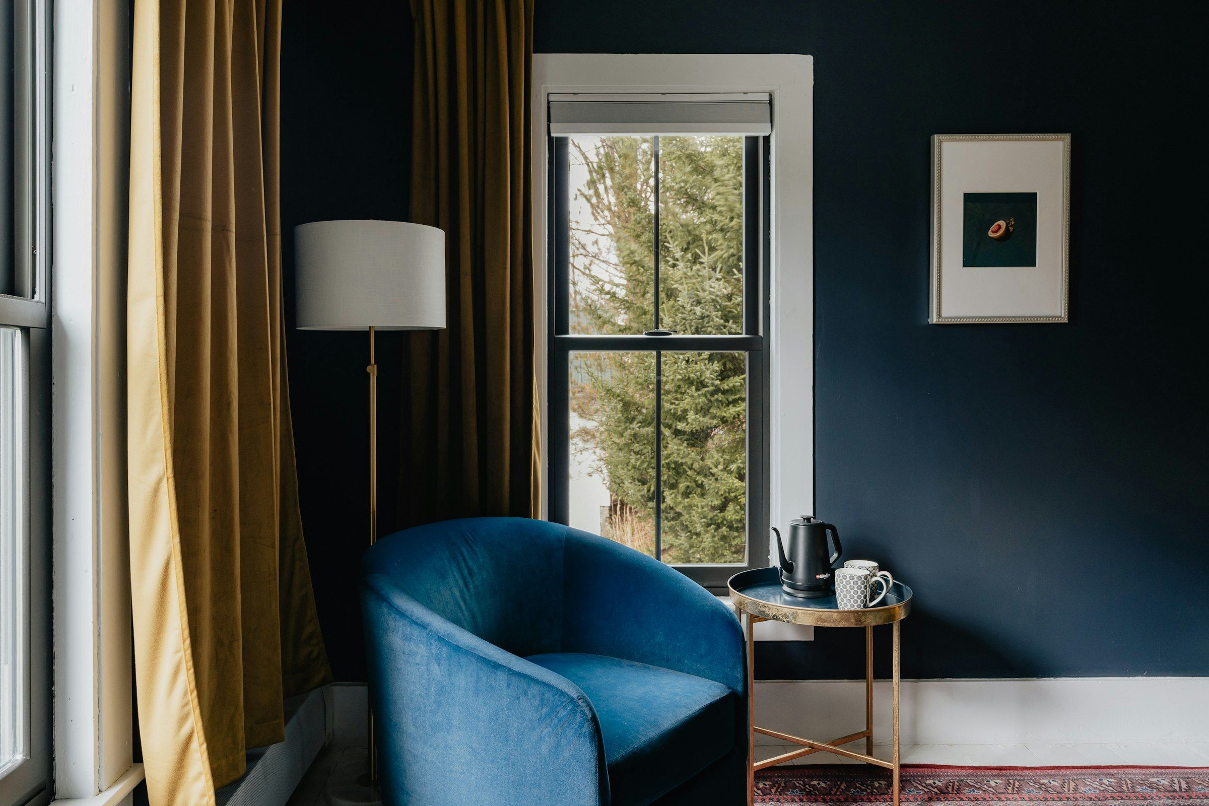 A blue armchair and a floor lamp beside a tall window in a dark blue room