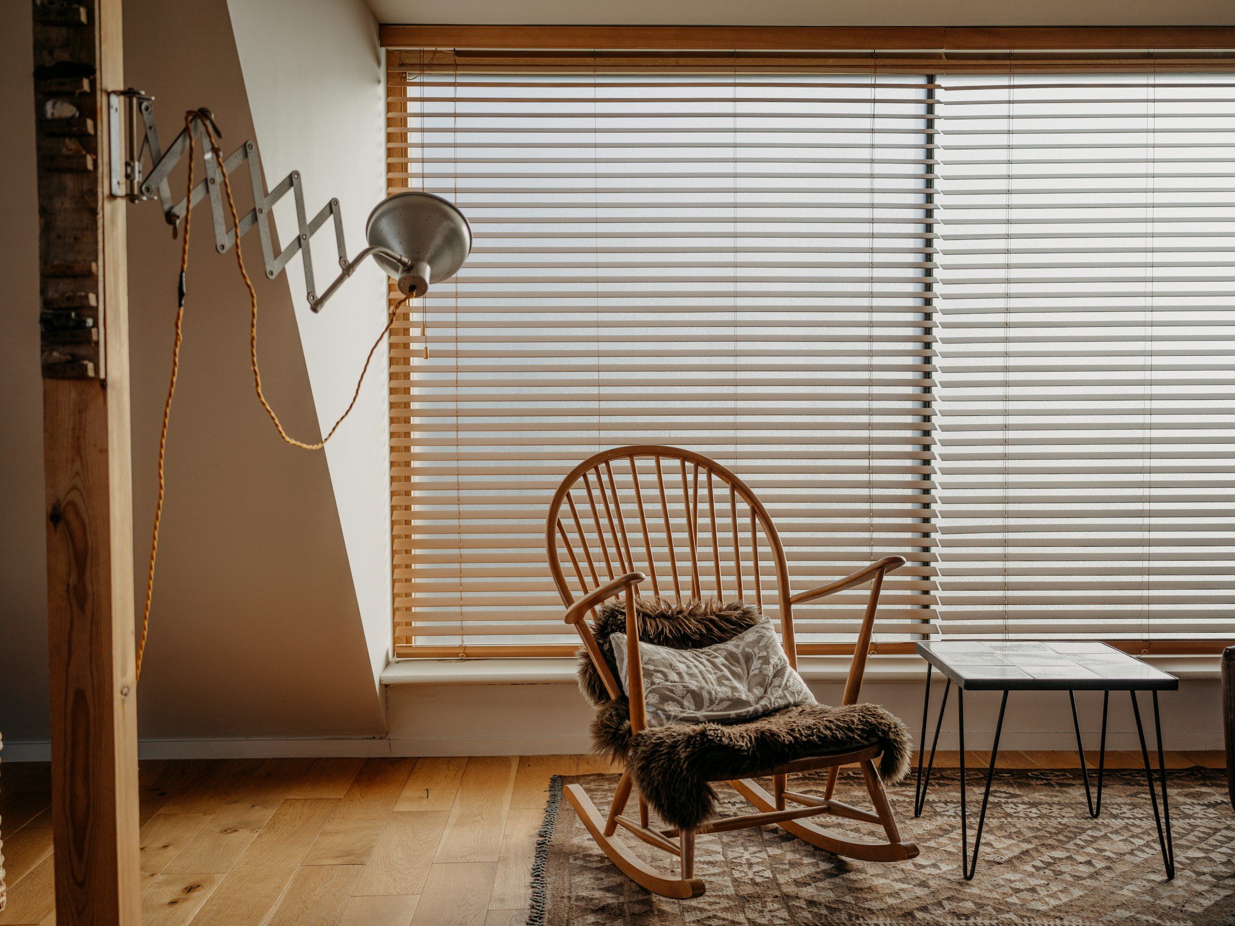 A wooden rocking chair beside a window with half-open blinds
