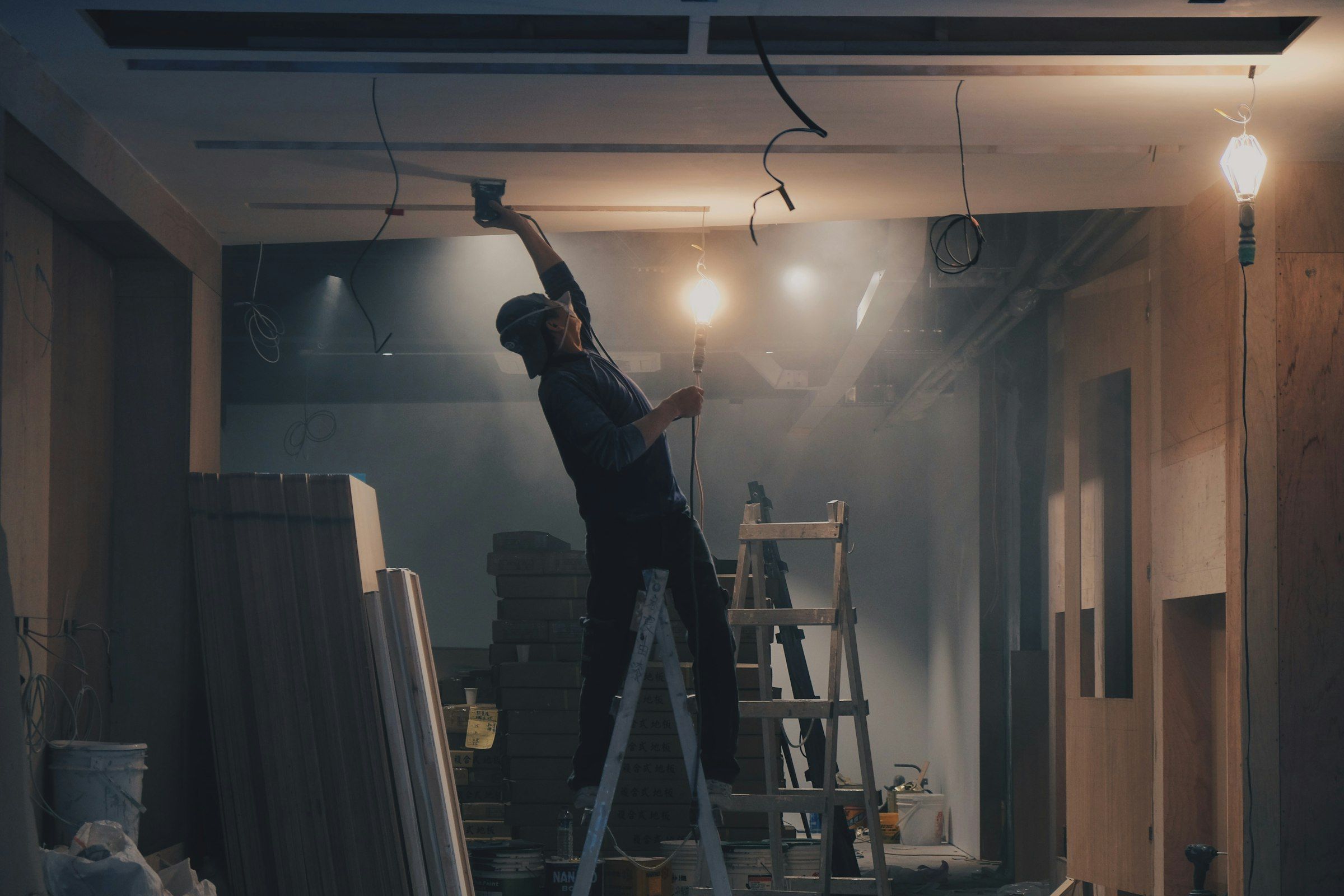 A worker on a ladder fitting a ceiling in a room under construction