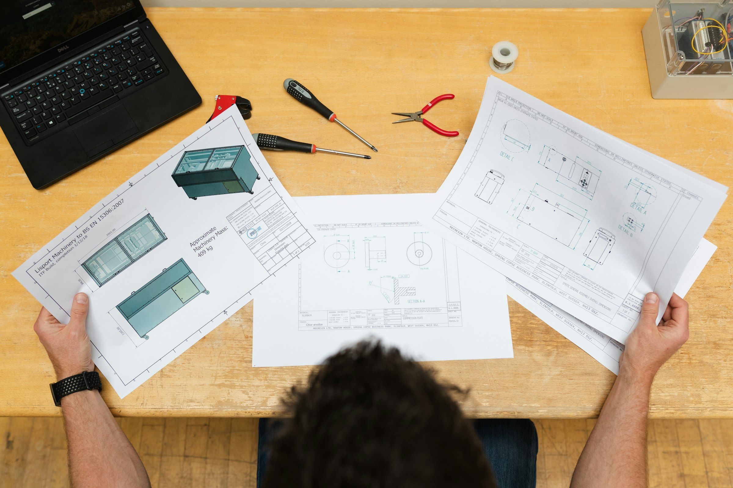 Hands spreading printed plans and cabinet drawings across a wooden table