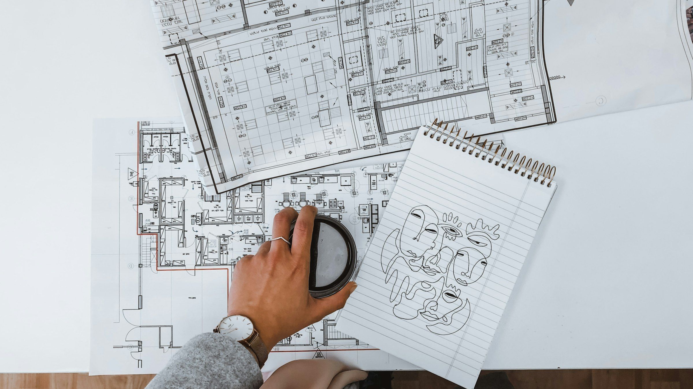 A hand working over printed floor plans beside a sketchbook
