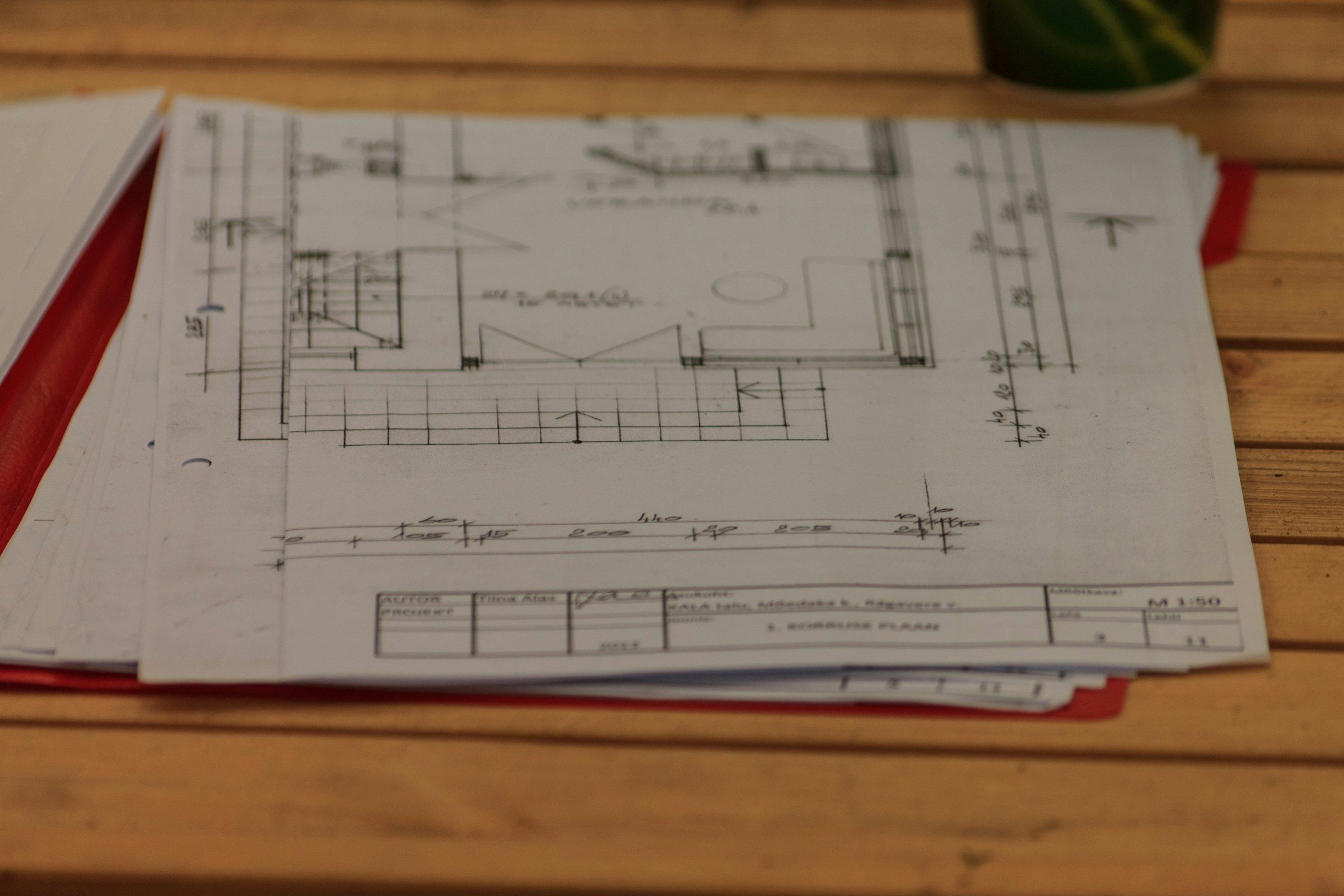 A stack of printed construction drawings with a title block on a wooden table