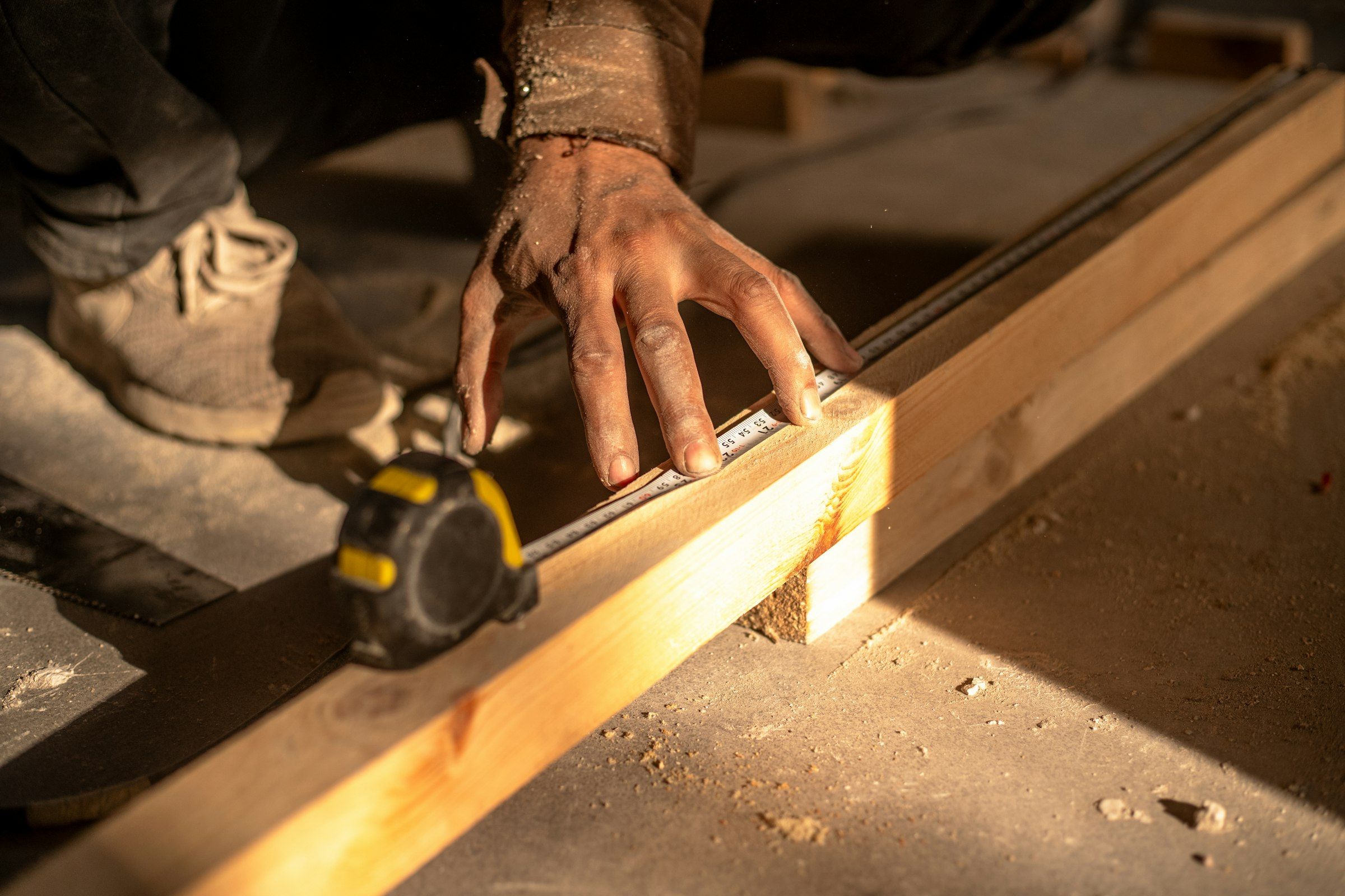 A tape measure held against a length of lumber on a dusty floor