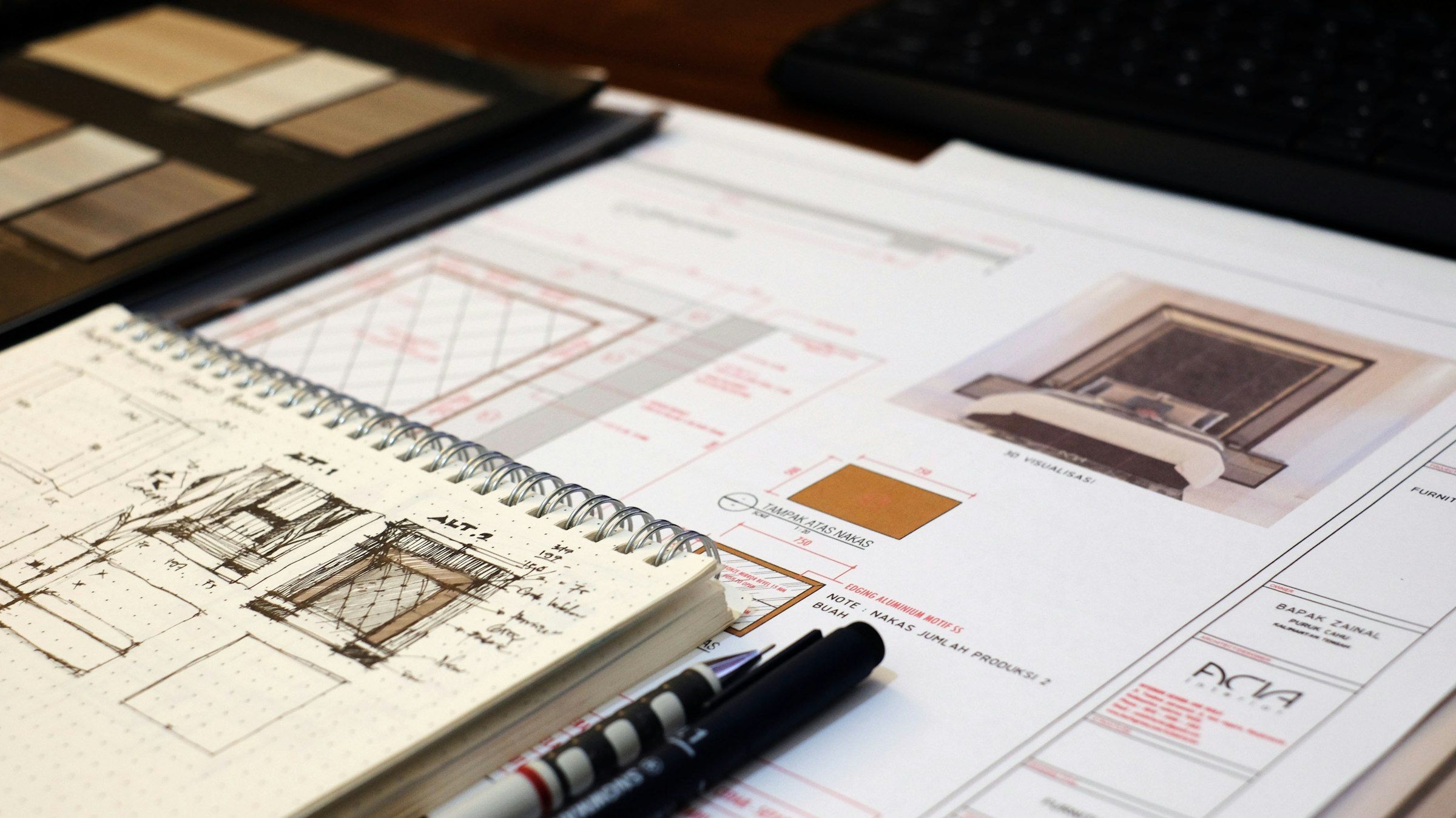 Design sketches in a notebook beside printed drawings and material samples
