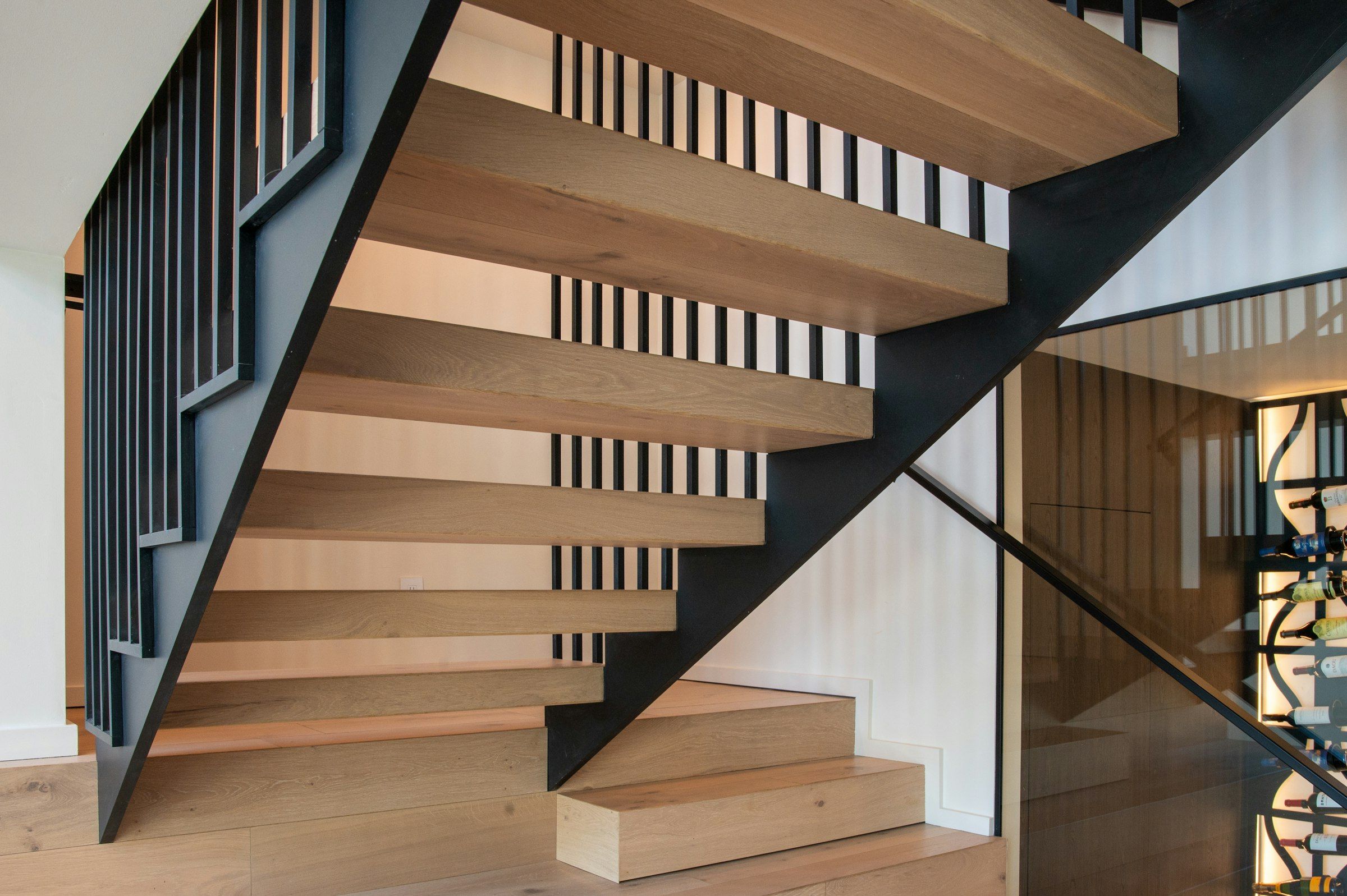 A white-oak floating staircase with a black steel rail