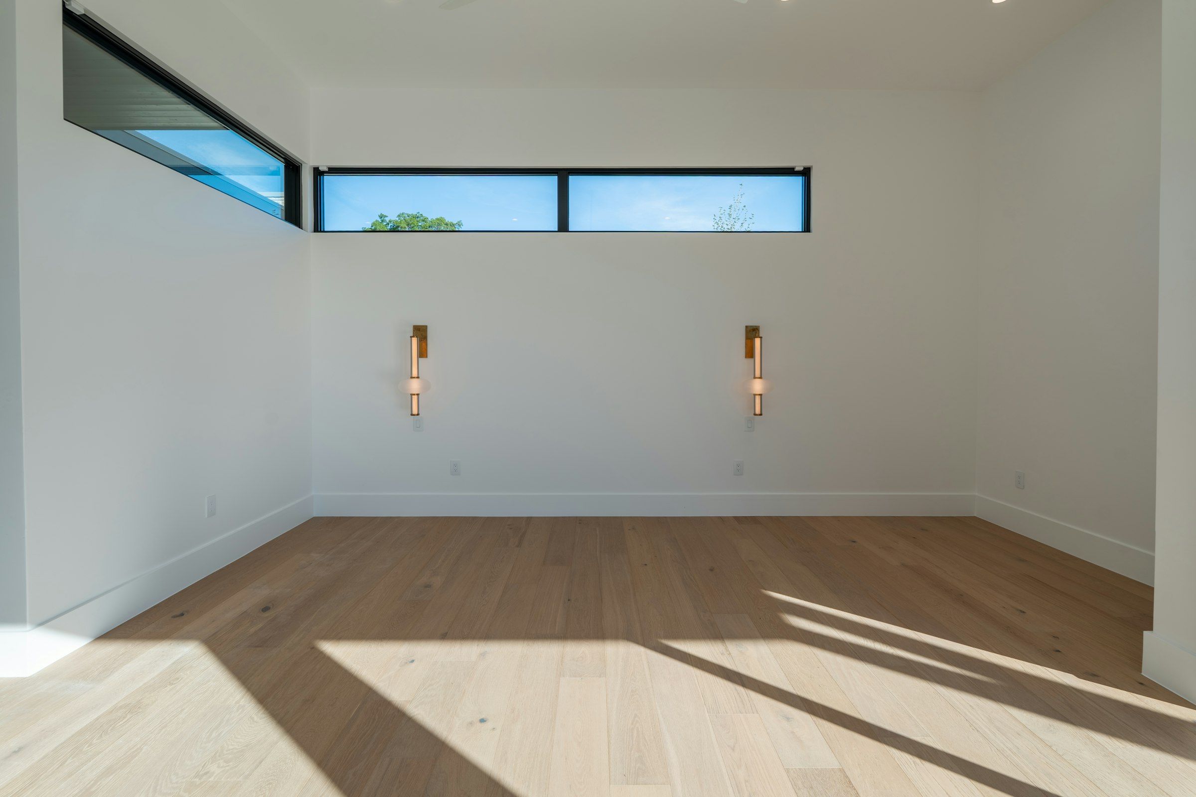 Wide-plank light oak flooring in sunlight below a band of high windows