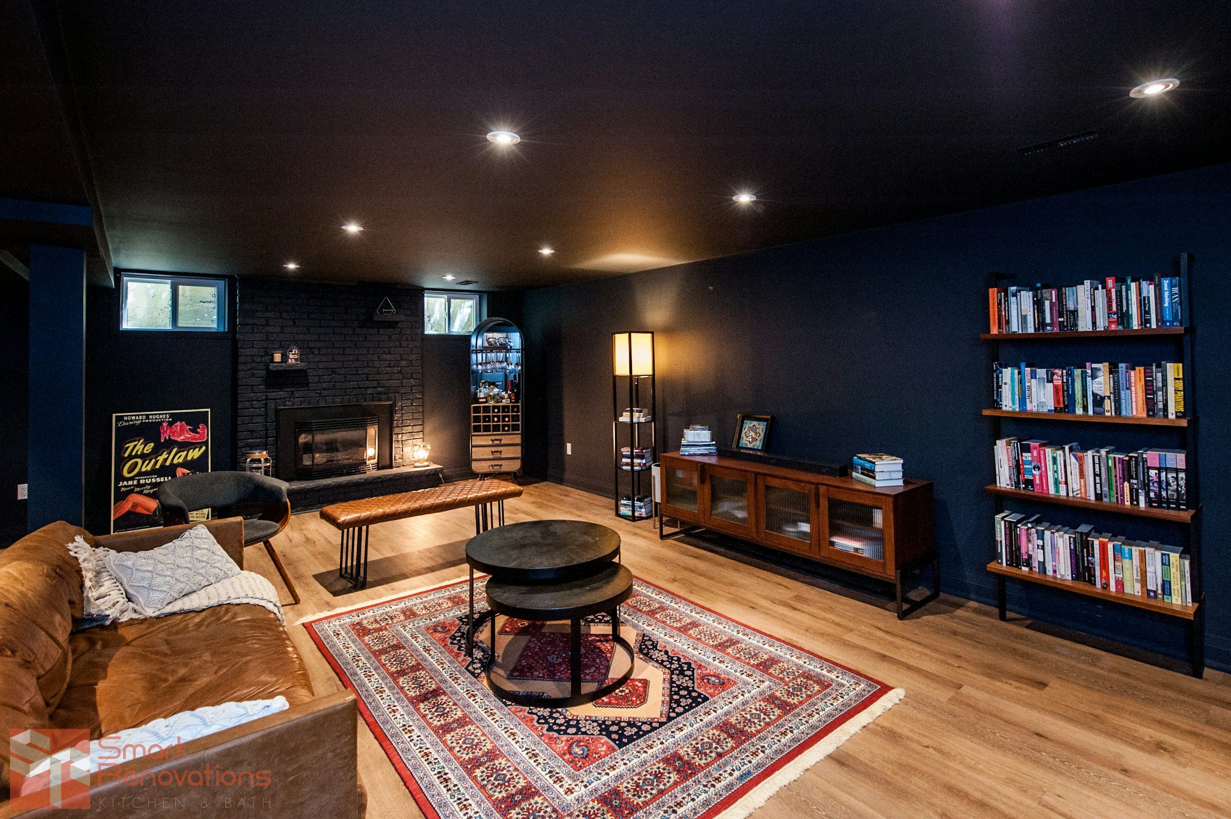 A finished basement lounge with a dark ceiling, a brick fireplace, bookshelves and a leather sofa