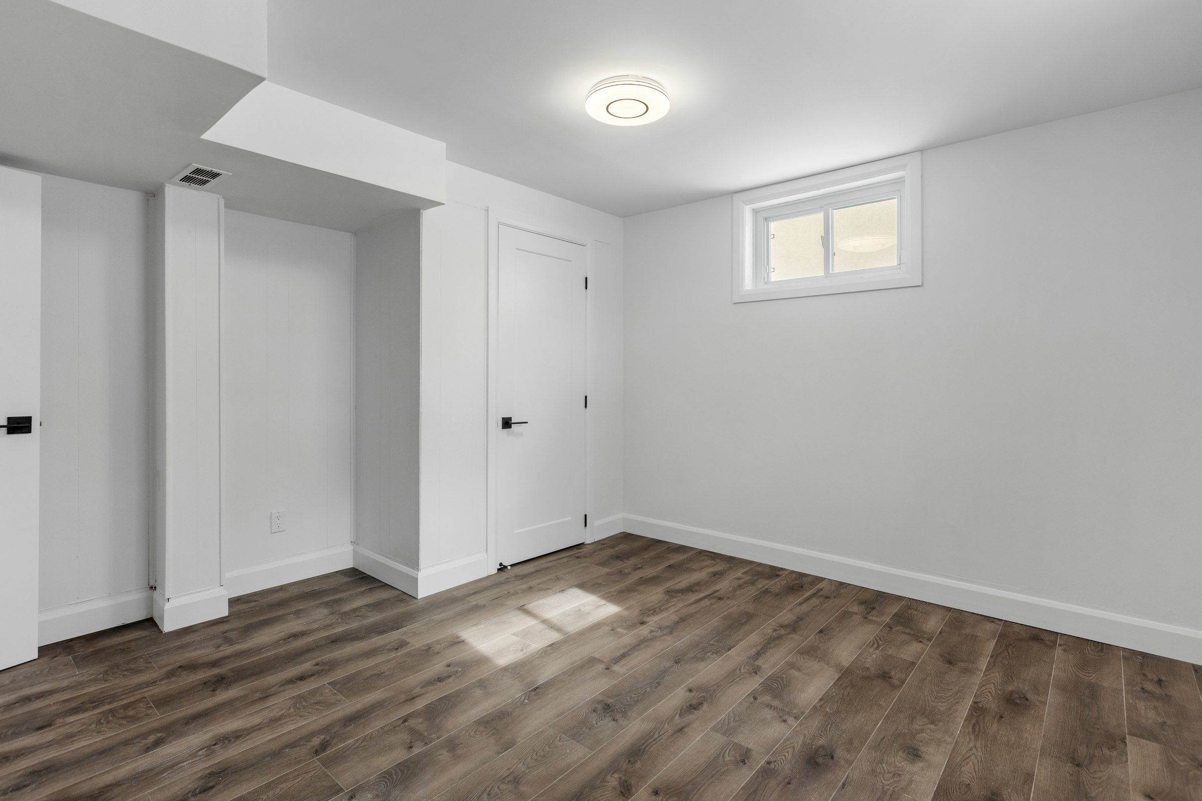 An empty finished basement bedroom with a small window high on the wall