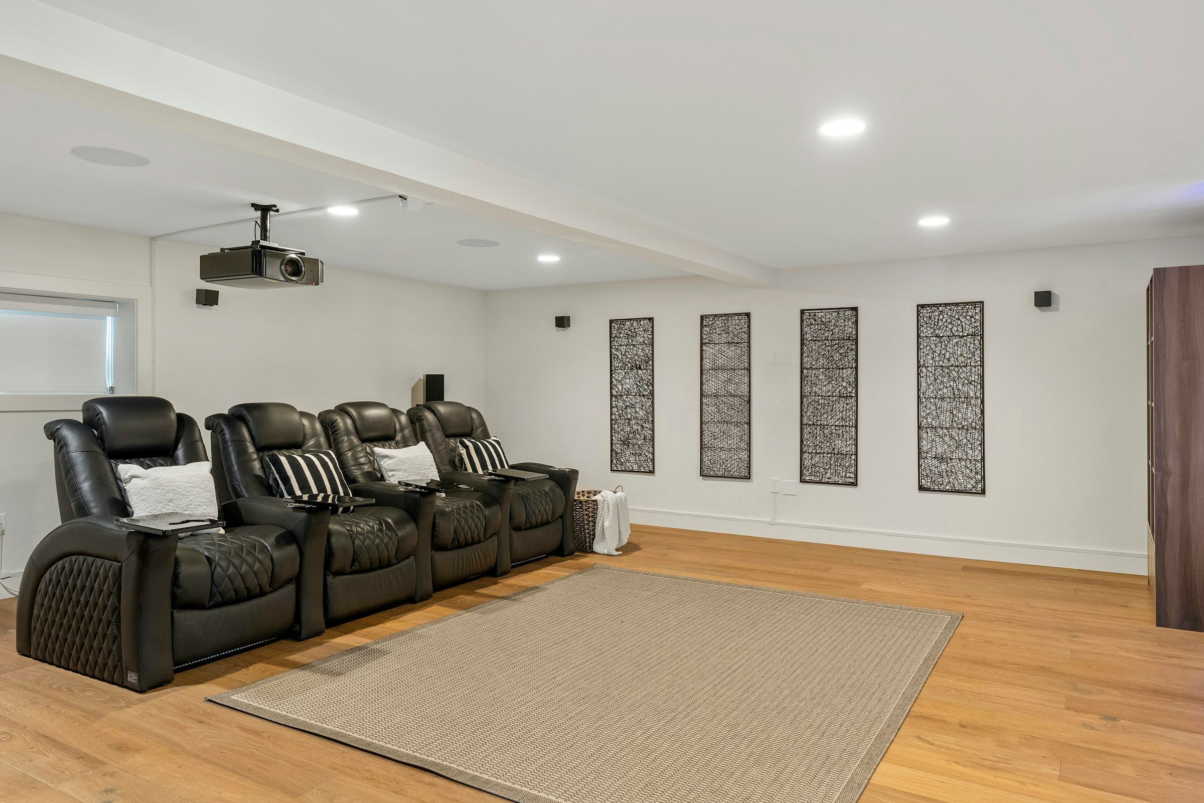 A basement media room with a row of leather recliners, a ceiling projector and acoustic wall panels